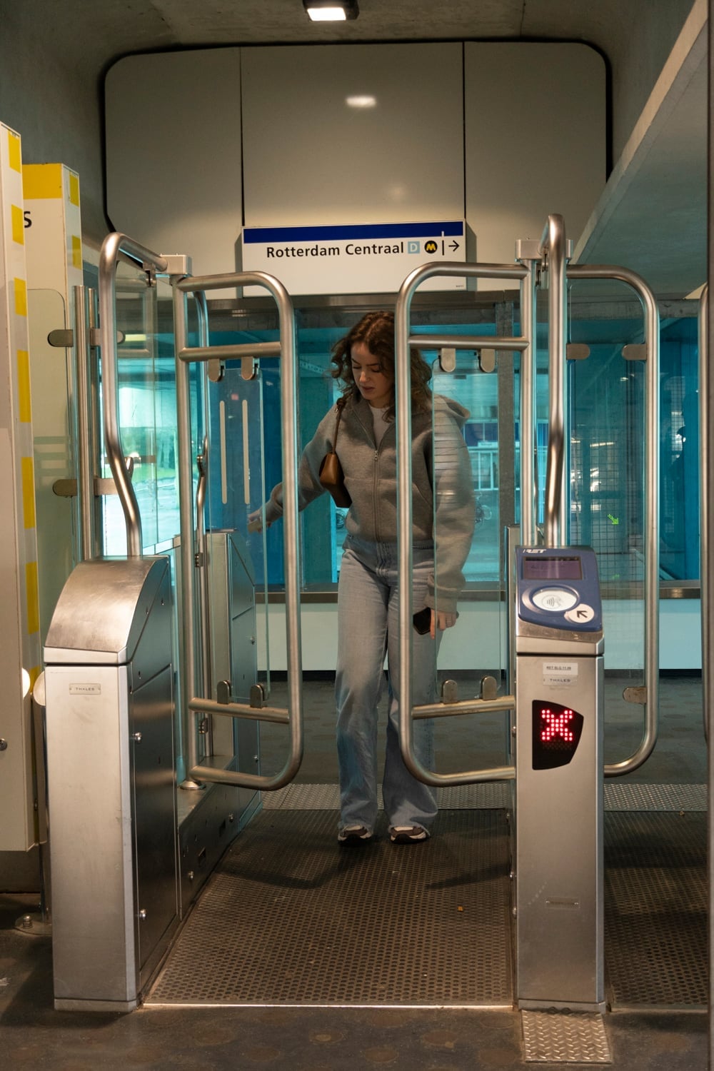 Vrouw loopt door de OV-poortjes onder een bord met Rotterdam Centraal, met een rood kruis op het display naast haar.