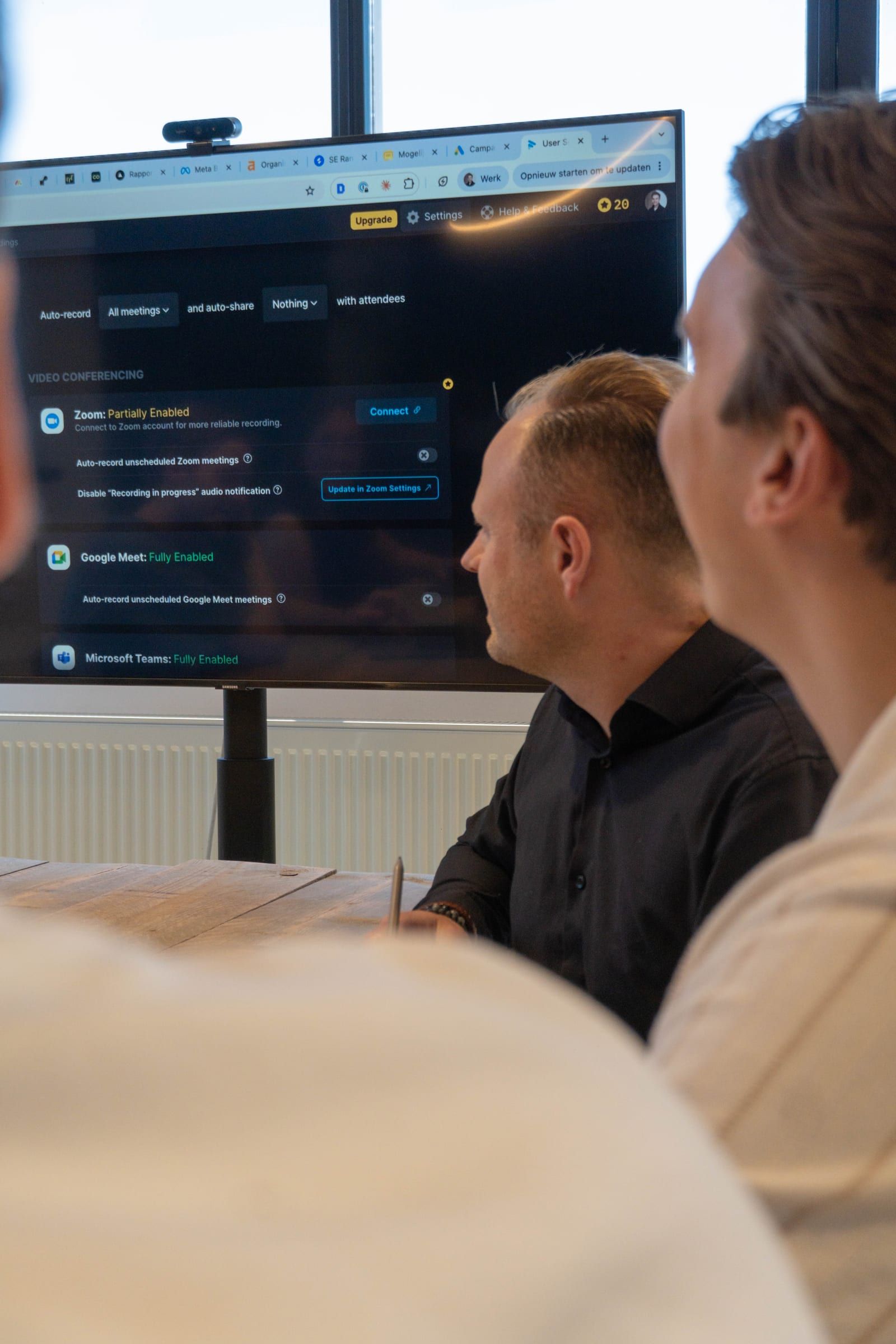 Twee collega's kijken naar een groot scherm met een instellingenpaneel voor videovergaderen.